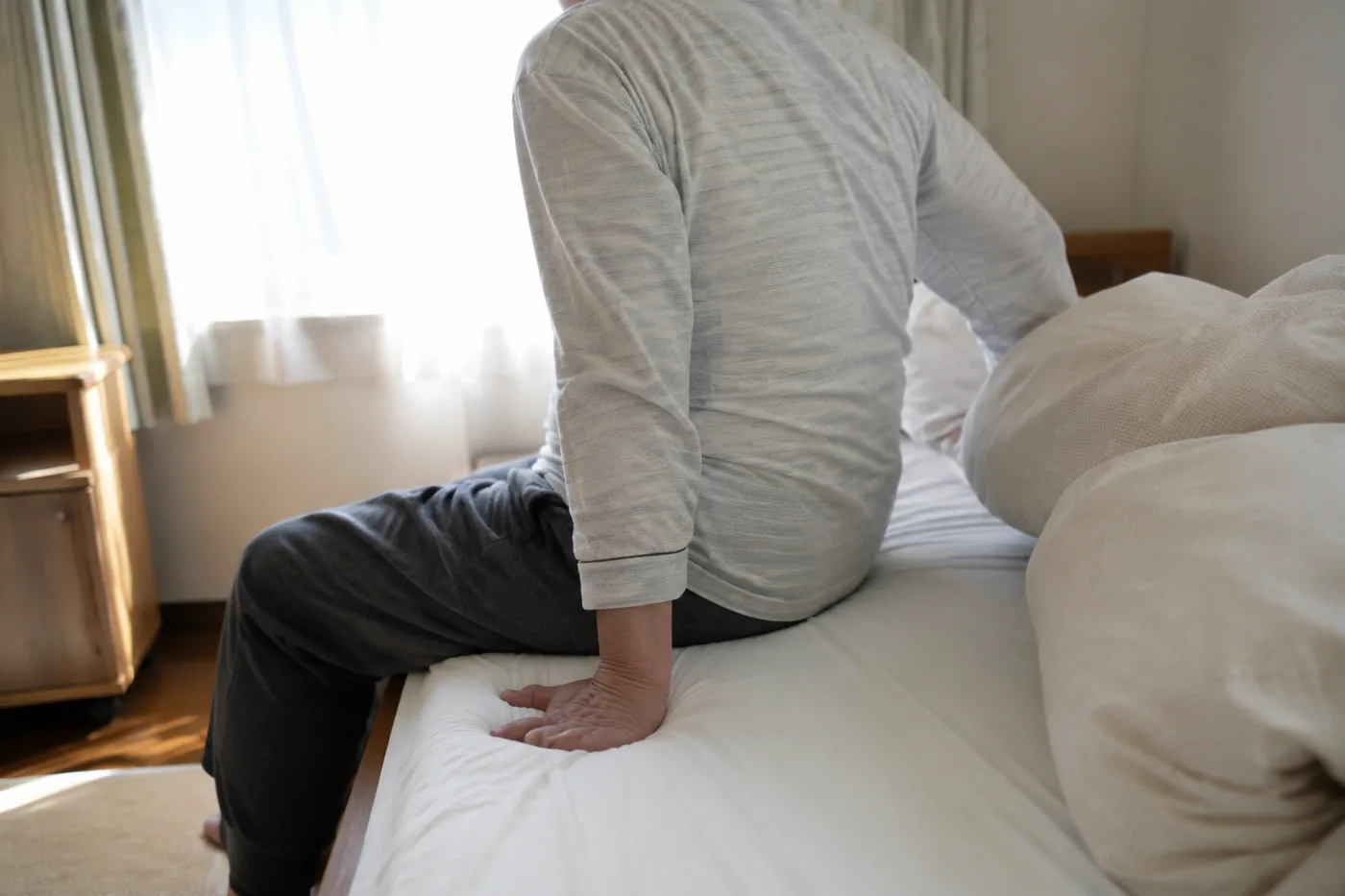 ベッドの上で、横を向いて手をつきながら起き上がろうとしている高齢の男性